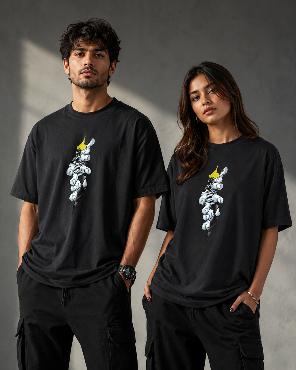 A man and a woman modeling matching black graphic t-shirts featuring a white cartoon rabbit wearing a yellow crown, set against a dark gray textured studio background.