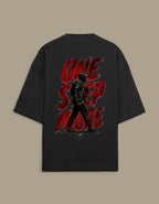 A black oversized t-shirt shown from the back, featuring a large graphic print with the words 'ONE STEP MORE' in distressed red lettering and a dark soldier silhouette.