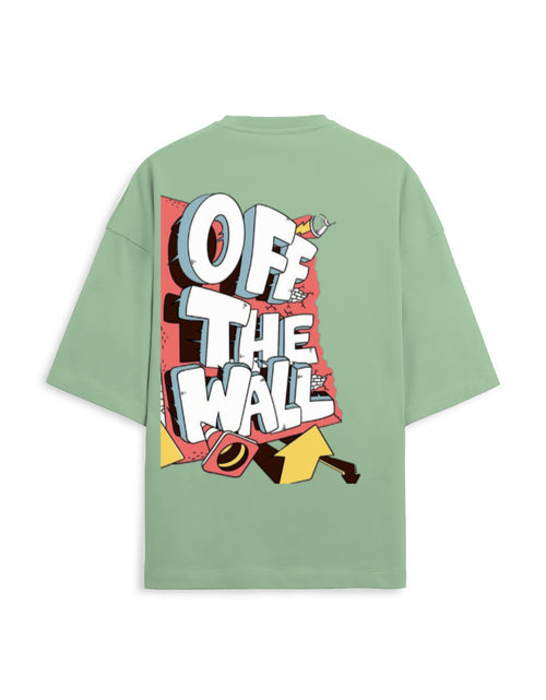 A sage green oversized short-sleeve t-shirt shown from the back, featuring a large graphic print with the words 'OFF THE WALL' in bold white letters over a red, yellow, and black comic-style illustration.