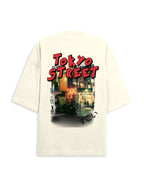An oversized cream-colored t-shirt shown from the back, featuring a large graphic print of a Tokyo street scene with 'TOKYO STREET' written in bold red letters.