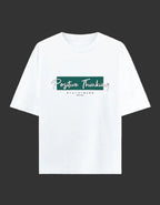 A white short-sleeve crewneck t-shirt with a graphic on the chest that reads 'Positive Thinking' in white script over a dark green rectangular block, with 'STAY STRONG' printed below in small black letters, displayed on a light cream background.