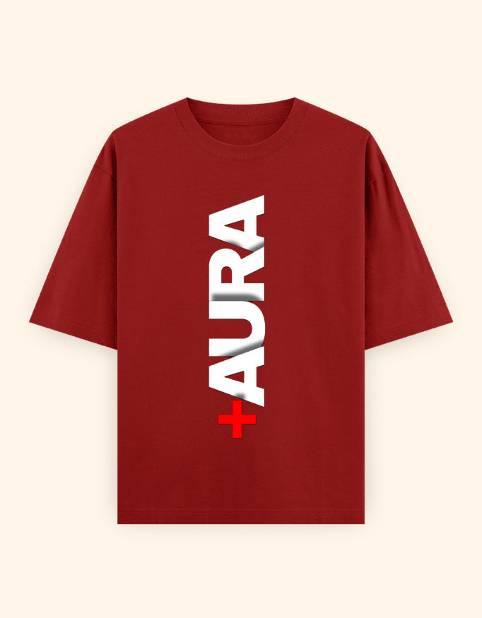 A red short-sleeve t-shirt with a vertical white 'AURA' text graphic and a small red cross symbol on the front, displayed against a light cream background.