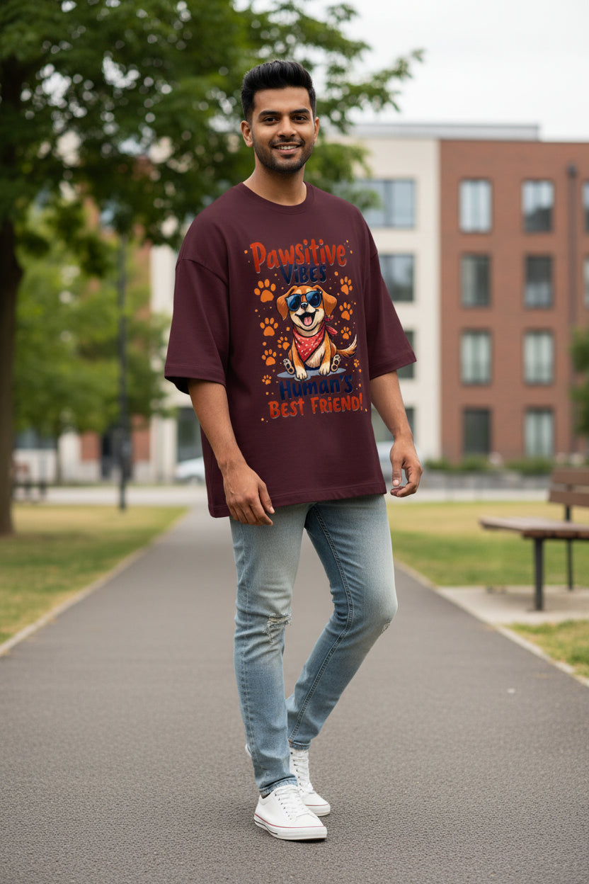 A dark maroon short-sleeve t-shirt with a colorful graphic of a cartoon dog wearing sunglasses and a bandana, surrounded by paw prints and the text 'Pawsitive Vibes Human's Best Friend!'.