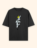 A black short-sleeve crewneck t-shirt featuring a graphic print of a hand tearing open the fabric to reveal a white and gray skeletal hand with a yellow crown, set against a solid cream background.