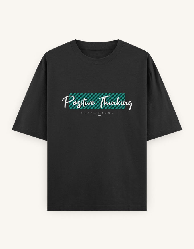 A black short-sleeve t-shirt with a 'Positive Thinking' graphic on the chest, featuring a teal textured block and white script text, displayed against a light off-white background.