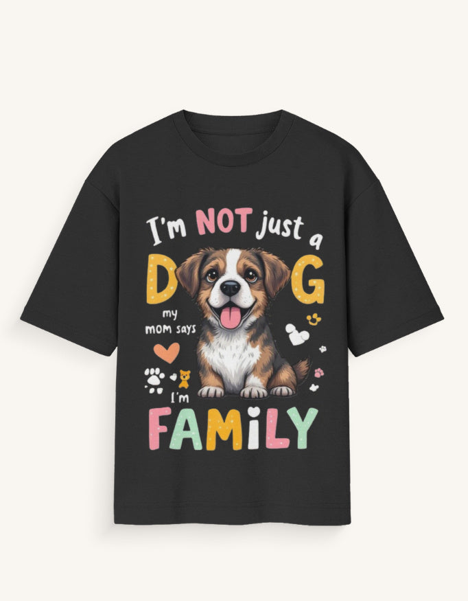 A black short-sleeve t-shirt with a colorful graphic print featuring a brown and white dog and the text 'I'm NOT just a D G my mom says I'm FAMILY' in pastel colors, shown against a light off-white background.