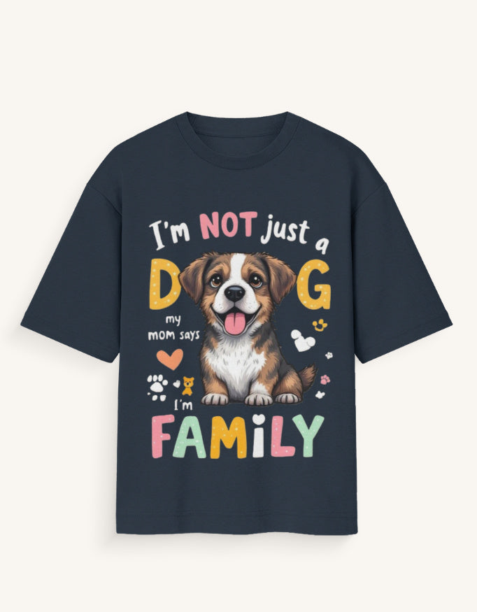 A navy blue short-sleeve t-shirt with a colorful graphic print featuring a dog and the text 'I'm NOT just a DOG my mom says I'm FAMILY', shown against a light cream background.