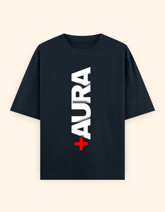 A navy blue short-sleeve t-shirt with a vertical graphic print reading 'AURA' in white block letters, with a small red cross symbol at the bottom, displayed on a light cream background.