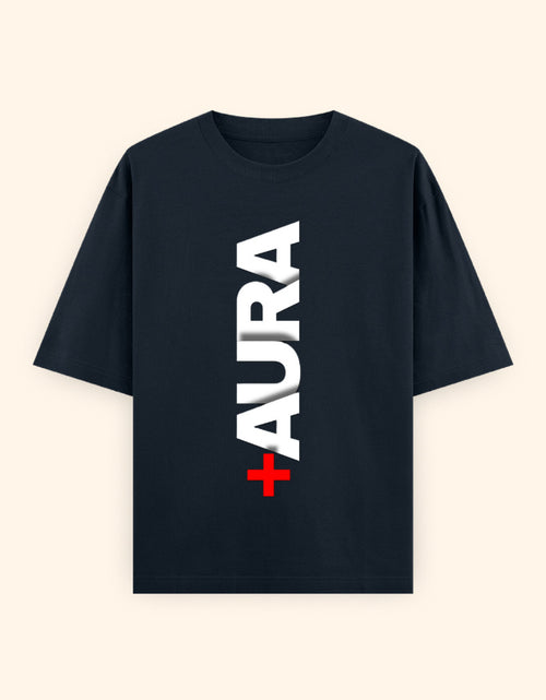 A navy blue short-sleeve t-shirt with a vertical graphic print reading 'AURA' in white block letters, with a small red cross symbol at the bottom, displayed on a light cream background.