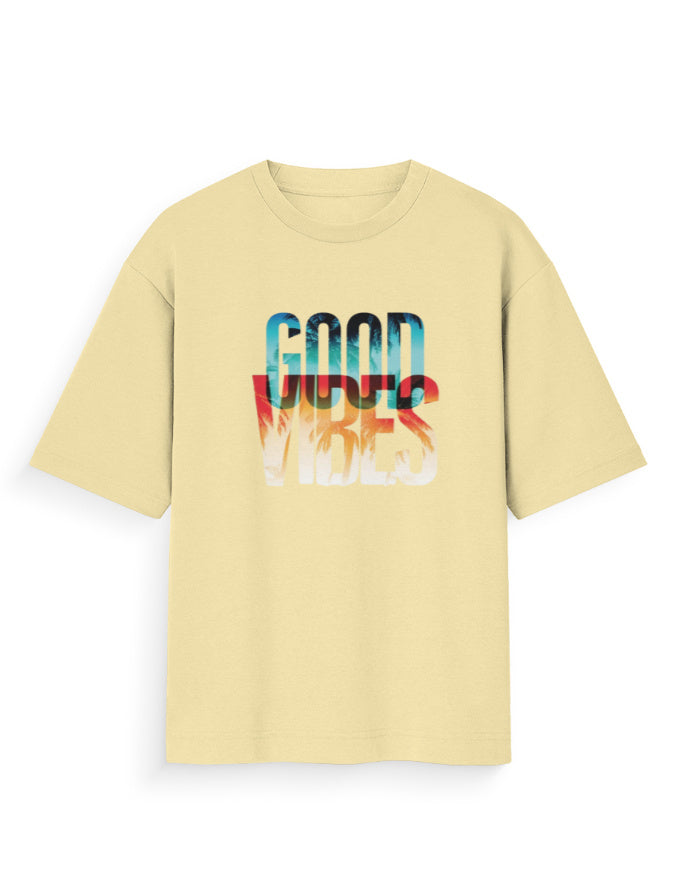 A pale yellow short-sleeve t-shirt with a colorful graphic on the chest reading 'GOOD VIBES' in a layered gradient of blue, red, and white.
