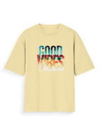 A pale yellow short-sleeve t-shirt with a colorful graphic on the chest reading 'GOOD VIBES' in a layered gradient of blue, red, and white.