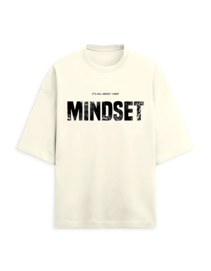 An oversized cream-colored t-shirt with a black distressed graphic on the front that reads 'MINDSET' with smaller text above reading 'IT'S ALL ABOUT YOUR'.
