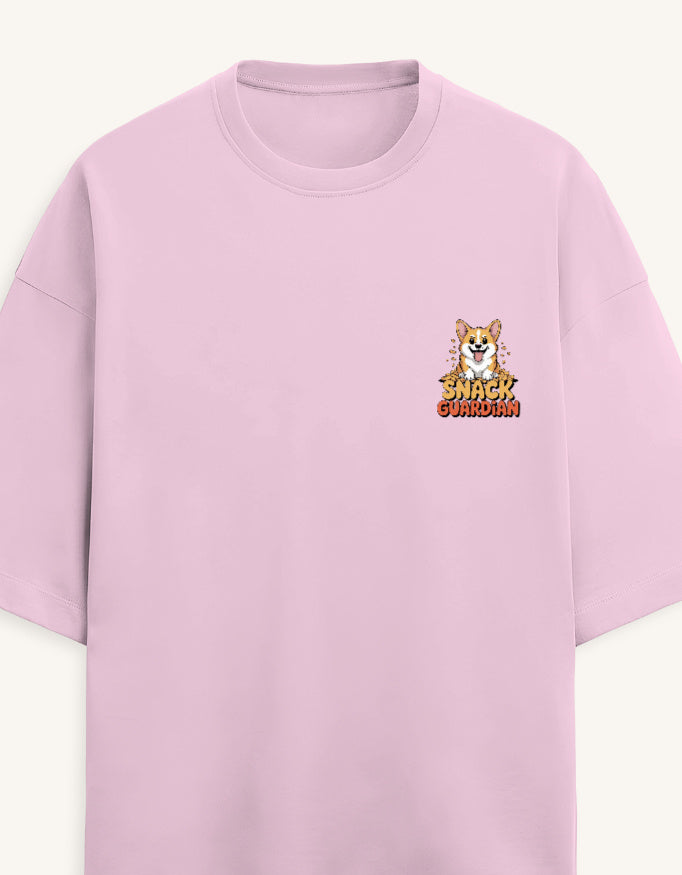 A light pink short-sleeve crewneck t-shirt featuring a small graphic on the left chest of a cartoon Corgi with the text 'SNACK GUARDIAN' in a retro font.