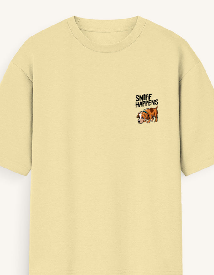 A pale yellow short-sleeve crewneck t-shirt with a small graphic on the left chest featuring the text 'SNIFF HAPPENS' above a cartoon dog face, shown against a light off-white background.