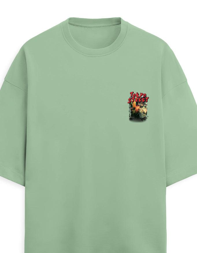 A sage green short-sleeve crewneck t-shirt with a small graphic print on the left chest featuring red stylized text and a fiery explosion design.