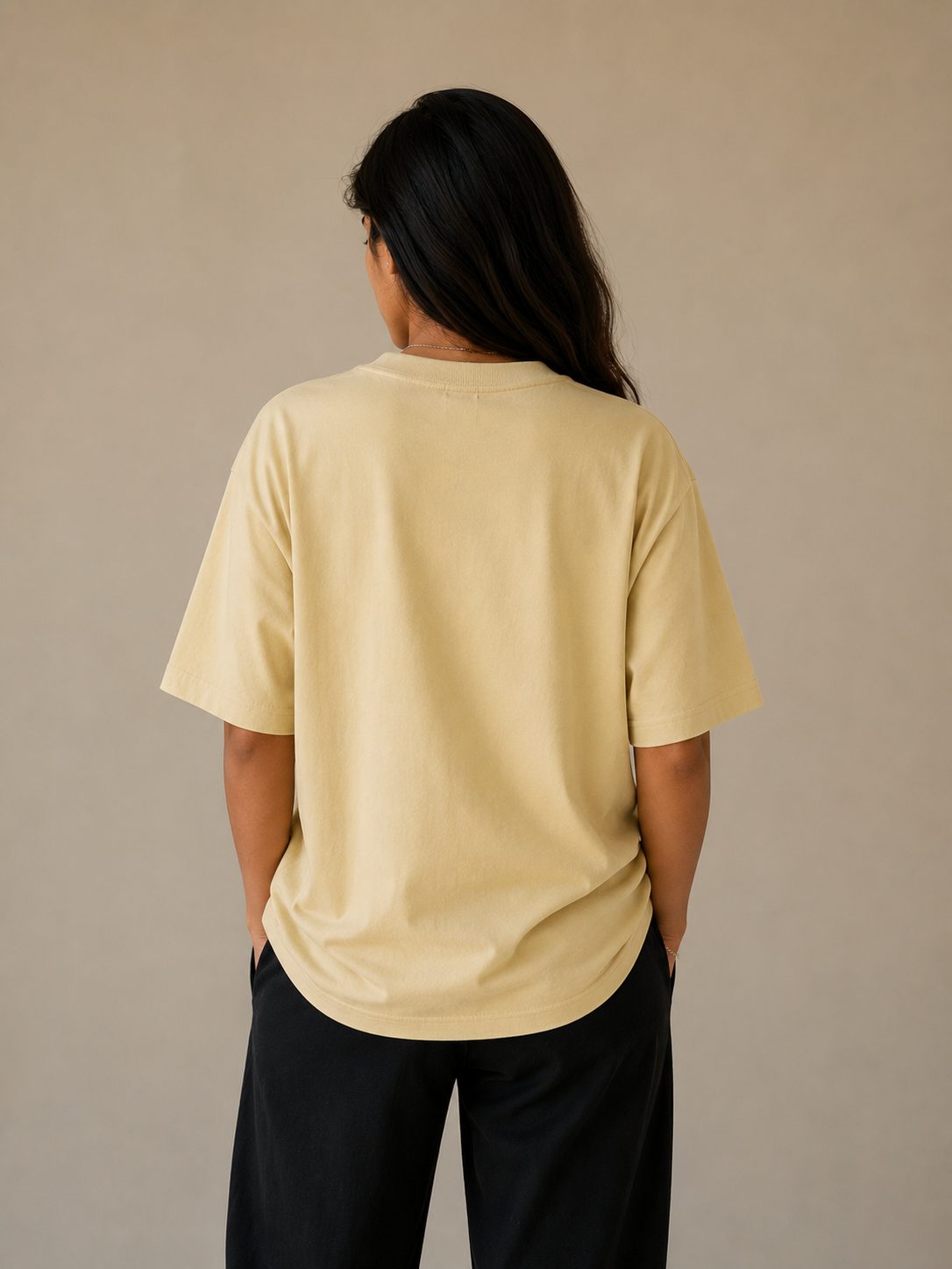 Person wearing a beige t-shirt and black pants against a beige background