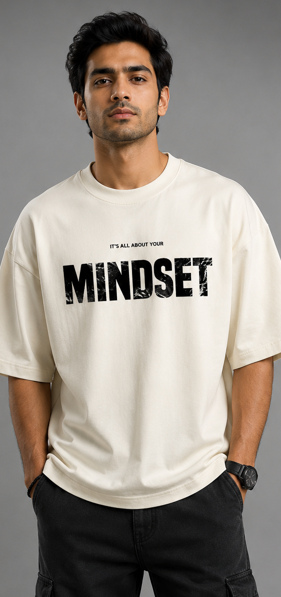 A man wearing an off-white crewneck t-shirt with a black distressed graphic that reads 'MINDSET' and smaller text above reading 'IT'S ALL ABOUT YOUR'.