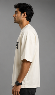 A man shown in profile wearing an oversized off-white t-shirt with a black graphic print on the left chest, photographed against a solid gray studio background.