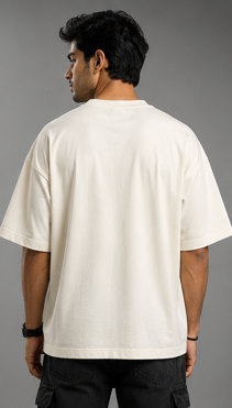A man viewed from the back wearing an oversized off-white short-sleeve t-shirt and black cargo pants against a solid gray studio background.