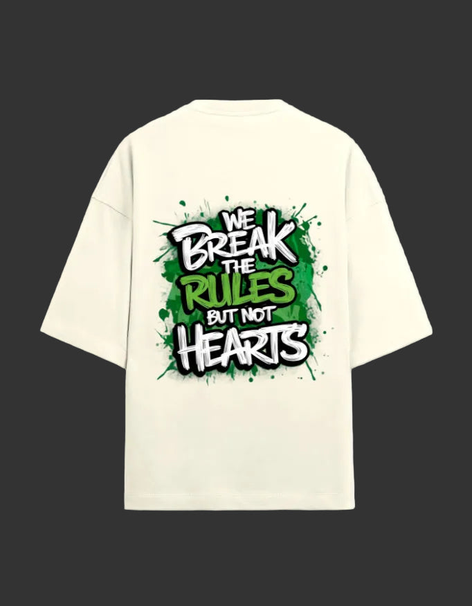 An off-white short-sleeve t-shirt shown from the back, featuring a bold graphic print with the text 'WE BREAK THE RULES BUT NOT HEARTS' in white, green, and black graffiti-style lettering over a green paint splatter background.