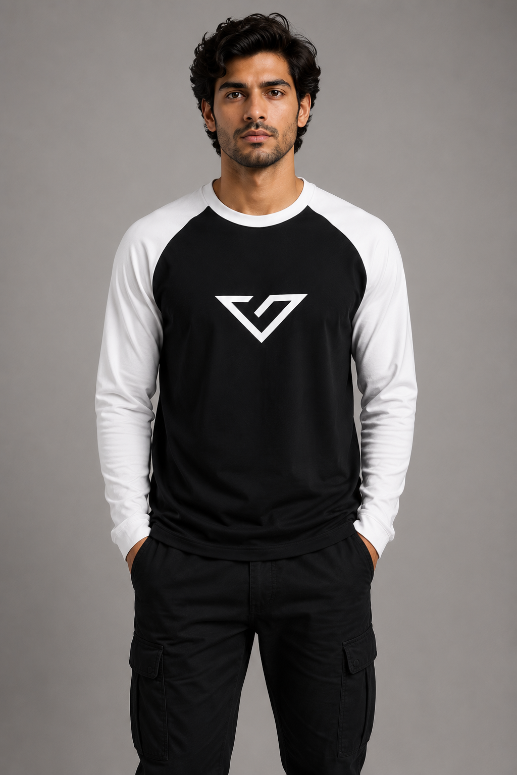 A man wearing a black and white raglan long-sleeve shirt with a white geometric logo on the chest, paired with black cargo pants, against a solid gray studio background.