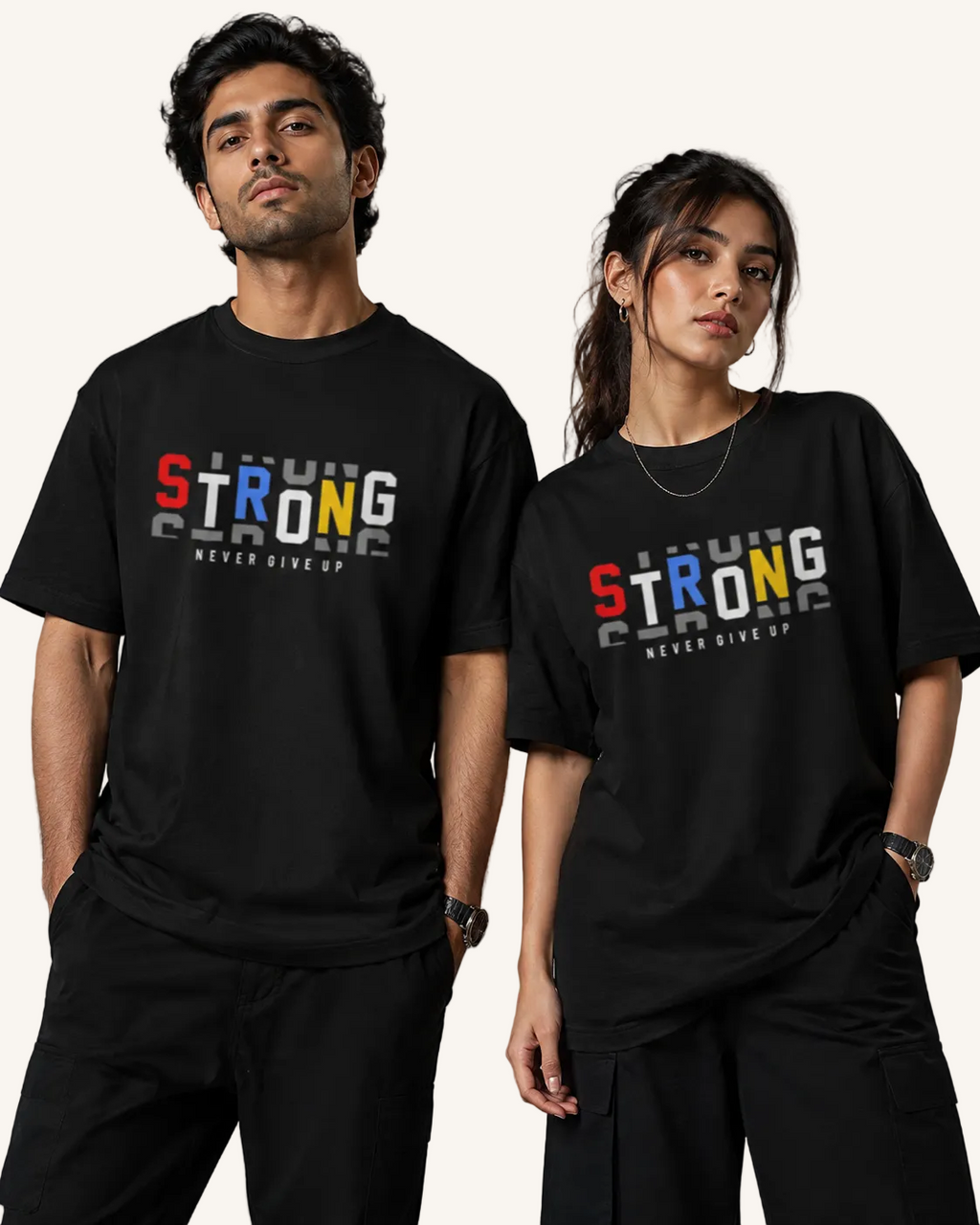A man and a woman modeling matching black graphic T-shirts against a neutral gray studio background. The shirts feature a colorful 'STRONG' graphic with 'NEVER GIVE UP' underneath.
