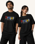 A man and a woman modeling matching black graphic T-shirts against a neutral gray studio background. The shirts feature a colorful 'STRONG' graphic with 'NEVER GIVE UP' underneath.