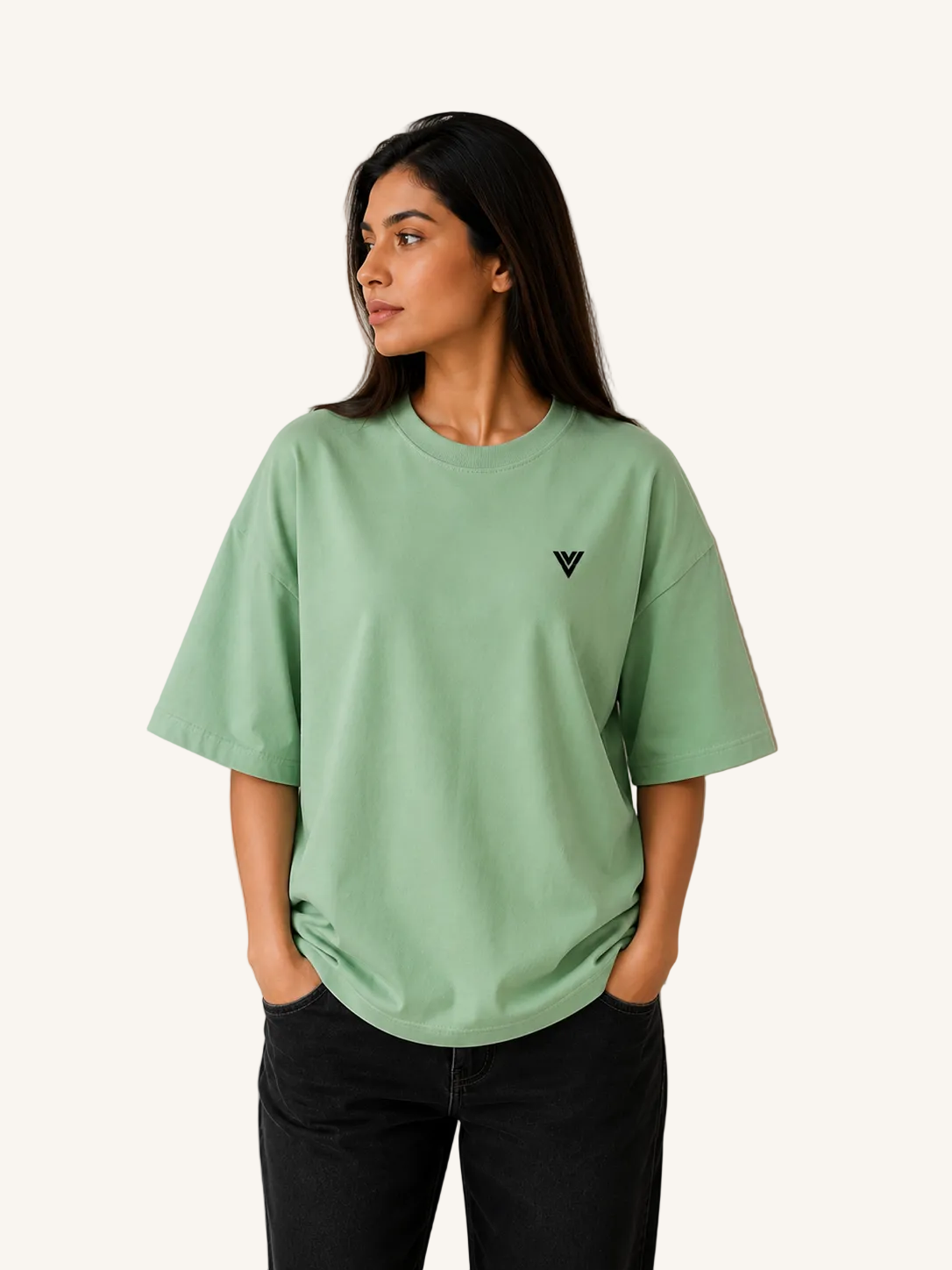 Woman wearing a light green t-shirt with a small black logo against a beige wall.